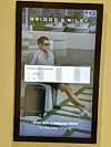 Electronic sign with pop-up text 'Biz Daemon is not responding' over an image of a man in shorts sitting on a wall with a wheeled suitcase