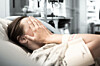 Woman in hospital (in hospital gown) covers face with hands