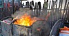 Dumpster fire against background of wooden fence with sad green recycling badged nailed to it