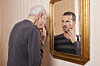 Older man looking at younger self in the mirror
