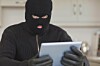 Burglar sits in kitchen with stolen tablet. Photo by Shutterstock
