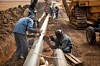 Welders wearing protective clothing fixing welding and grinding industrial construction oil and gas or water and sewerage plumbing pipeline outside on site. Photo by Andrea Slatter/Shutterstock