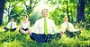 Business types meditate in green field. Photo via Shutterstock
