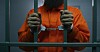 Someone in an orange jumpsuit in cuffs behind bars