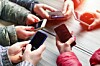 A group of people hold out mobile phones in a circle. Photo by Shutterstock