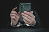 Photo of a scammer in cuffs holding a phone
