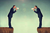 Two businessmen facing each other shouting into loudhailers