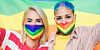 Two people wearing LGBTQ pride masks with a flag behind them