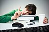 staffer props head on pile of books as he clicks a mouse and fights sleep