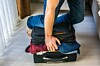 person sitting on suitcase to force it closed