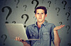 A man shrugs at a laptop with a background of question marks