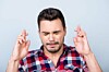 Man closes his eyes and crosses fingers
