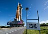Artemis II SLS heading to the launchpad with 'Drive Safely' sign in the foreground
