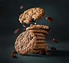 Oatmeal raisin cookies falling onto a stack with scattered raisins on a dark surface
