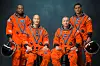 Four astronauts in orange spacesuits pose holding black helmets against a dark background.