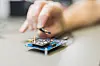 Qualinx QLX3xx chip held in tweezers above a circuit board