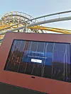 Tilted kiosk screen shows an app error message in front of roller coaster tracks.