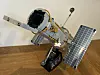 Lego Hubble Space Telescope model with open panels on a stand against a plain wall.