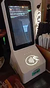 Payment terminal on a bar counter showing a terminal screen and illuminated contactless symbol.