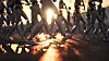 Silhouetted armed robots march in formation across wet ground at sunset.