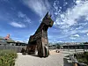 Large wooden horse sculpture outdoors beneath a partly cloudy sky.