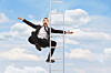 A frightened businessman in a suit falls beside a metal ladder against a blue sky with clouds.