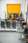 Rows of small satellites on assembly carts inside a bright industrial facility.